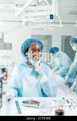 Giovane felice donna affascinante medico in cuffia e maschera viso ha eseguito operazione di successo, lavoro preferito Foto Stock