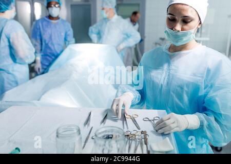 carino assistente femminile scelta dello strumento per la chirurgia in ospedale. primo piano foto. medici che lavorano in background sfocato Foto Stock