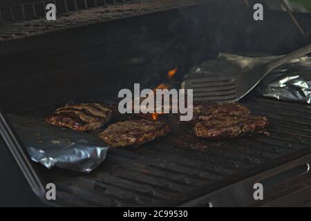 persona che capovolge hamburger al barbecue con le fiamme Foto Stock