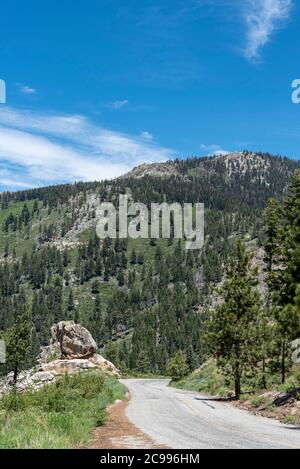 Stretta strada di montagna che scende in collina, sotto il cielo blu con le nuvole bianche. Foto Stock