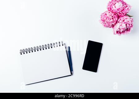 Spazio di lavoro femminile disposizione piatta notebook vuoto con telefono cellulare accanto al bouquet di fiori freschi su tavolo bianco, vista dall'alto. Foto Stock