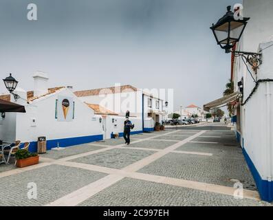 La piazza principale con la gente che si rilassa ai caffè a Picturreche Porto Covo in Portogallo Foto Stock