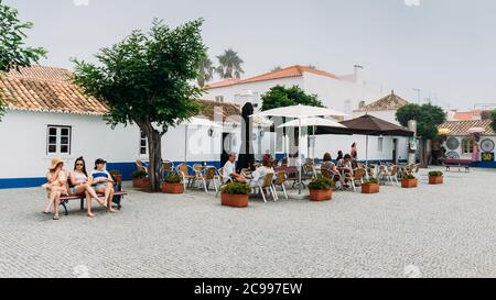 La piazza principale con la gente che si rilassa ai caffè a Picturreche Porto Covo in Portogallo Foto Stock