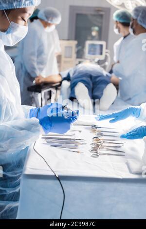 L'infermiera s mani strumenti chirurgici e strumenti, close up compreso il bisturi, pinze e pinzette a molla disposti su una tavola. Chirurghi al lavoro in opera Foto Stock