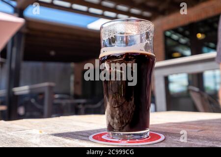 Una birra artigianale scura, una stout, in una chiara pinta di vetro seduta su una montagna rossa e bianca. Foto Stock