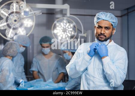 Chirurgo indiano sicuro guardando la macchina fotografica in ospedale della stanza chirurgica, medico indossa il vestito di scrub di chirurgia verde. Foto Stock