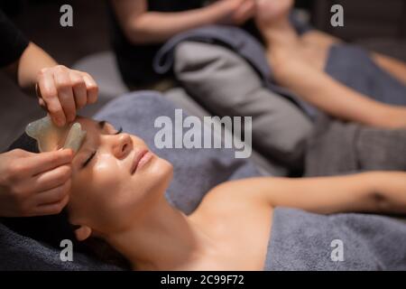 le donne ricevono un massaggio viso. cura della pelle e del corpo. due donne caucasiche ricevono un massaggio al salone di bellezza Foto Stock