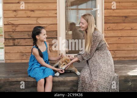 Madre felice seduta sul portico insieme con sua figlia e giocano con il cane Foto Stock
