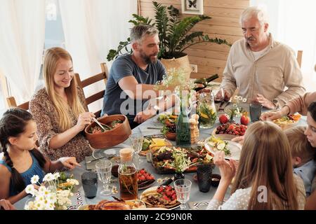Felice famiglia seduta a tavolo festivo insieme e mangiare diversi piatti a casa Foto Stock