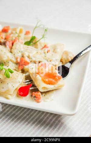 Un primo piano di pasta di paccheri con salsa di panna e salmone su una forchetta, su un piatto bianco Foto Stock