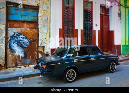 L'Avana, Cuba, luglio 2019, auto nera Lada 1600 parcheggiata accanto a un graffito che rappresenta una chimera nella parte più antica della capitale Foto Stock