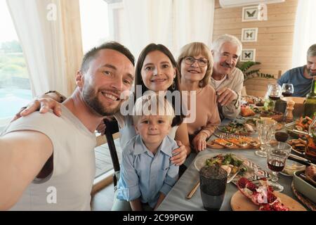Ritratto di uomo maturo che fa un ritratto selfie della sua grande famiglia mentre si siedono al tavolo durante la cena a casa Foto Stock