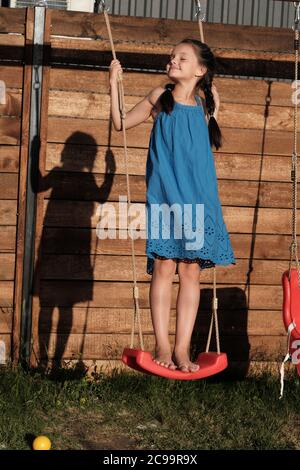 Carina bambina in abito blu giocando su un parco giochi all'aperto che dondola Foto Stock