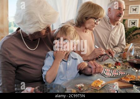 Nonna seduta al tavolo da pranzo con il nipote e nutrendolo a casa Foto Stock