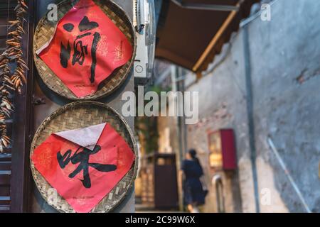 Chongqing, Cina - Agosto 2019 : caratteri cinesi scritti in inchiostro nero su sfondo rosso, all'interno di vassoi rotondi di vimini attaccati alla parete di a. Foto Stock