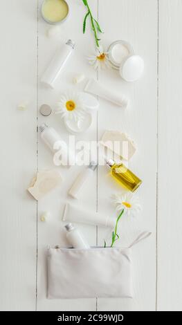 Set prodotti cosmetici in confezione bianca su tavolo di legno con fiori, sacchetto cosmetico. Bellezza cura della pelle trattamento dei capelli siero cosmetico olio idratante Foto Stock