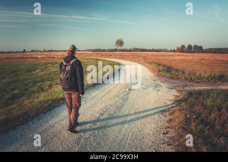 Un uomo con uno zaino va strada ghiaiata in un giorno d'autunno Foto Stock