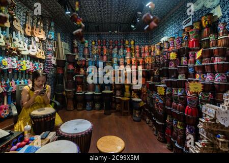 Feng Huang, Cina - Agosto 2019 : annoiato venditore femmina in attesa di clienti all'interno del suo strumento tradizionale e negozio musicale sulla strada in O Foto Stock