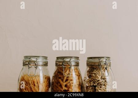 Tre contenitori in vetro pieni di ingredienti alimentari secchi non cotti. Riso, pasta, farina, zucchero. Foto Stock