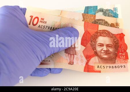 Moneta colombiana, banconote in pesos tenute in guanti di gomma. Il concetto di economia e minacce finanziarie durante l'epidemia di Coronavirus Foto Stock