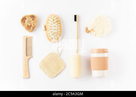 Articoli riutilizzabili eco-compatibili su superficie bianca. Spazzolino di bambù, spazzola per capelli detangenti, tazza di caffè, spugna esfoliante di loofah Foto Stock
