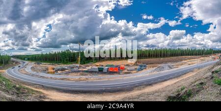 Umea, Svezia - 09 LUGLIO 2020: Vista panoramica sulla costruzione di nuove strade, lavori su nuovo ponte, gru a torre con molti container. Estate, foresta, vicino a um Foto Stock