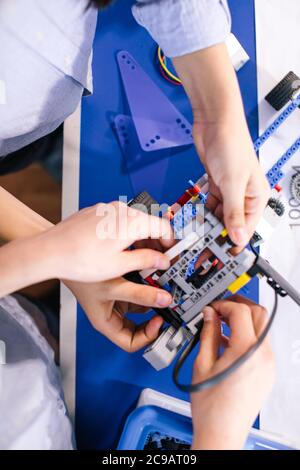 Primo piano delle mani dei ragazzi durante la creazione di un robot in laboratorio, lezioni di robotica. Sviluppo precoce, fai da te, innovazione, concetto di tecnologia moderna Foto Stock