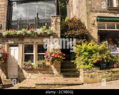 Cottage con conservatorio e negozio sulla strada principale nel villaggio di Howarth, West Yorkshire, in estate con finestre scatole, vasche e arbusti fuori Foto Stock