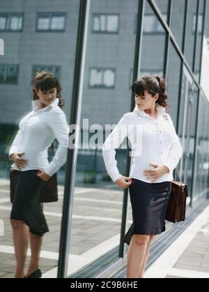 Donna matura perdere peso e guardando Mirror in Office Window Foto Stock
