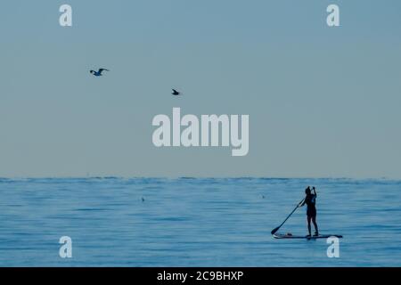 Worthing Beach, Worthing, Regno Unito. 30 luglio 2020. I paddleboarders godono del mare tranquillo del mattino. Con un cielo blu chiaro e acque piatte, le persone su tavole da paddle godersi la mattina presto al largo della costa del sussex. Rampion Wind Farm può essere visto 13-20km offshore. Foto per credito: Julie Edwards/Alamy Live News Foto Stock