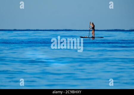 Worthing Beach, Worthing, Regno Unito. 30 luglio 2020. I paddleboarders godono del mare tranquillo del mattino. Con un cielo blu chiaro e acque piatte, le persone su tavole da paddle godersi la mattina presto al largo della costa del sussex. Rampion Wind Farm può essere visto 13-20km offshore. Foto per credito: Julie Edwards/Alamy Live News Foto Stock