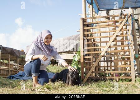 femmina musulmana coltivatore che alimenta animale in fattoria tradizionale Foto Stock