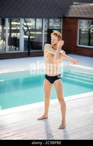 Uomo atletico a piedi nudi in costume da bagno vicino alla piscina Foto Stock