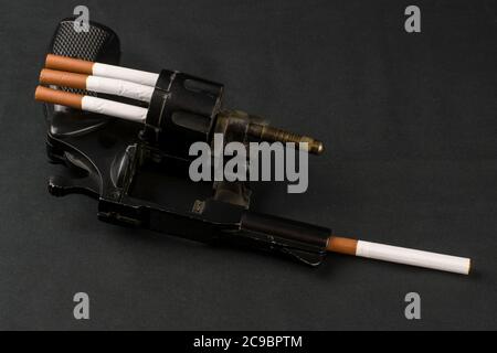concetto di danno al fumo, una sigaretta è caricata nel tamburo di un revolver, una sigaretta si stacca fuori dal barile una chiave scura Foto Stock