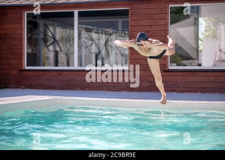 Uomo in berretto da bagno che spinge fuori dal bordo della piscina Foto Stock