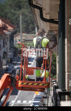 Operatore su una gru con un trapano che lavora in altezza in una sporgenza dell'edificio Foto Stock