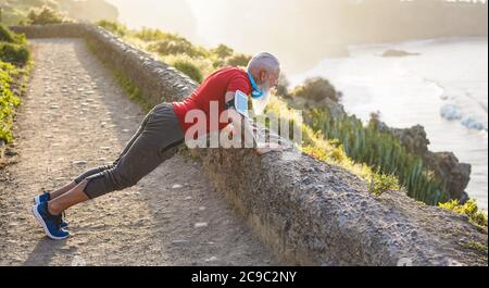 Uomo senior in forma che si allunga all'aperto al tramonto prima della sessione di allenamento - atleta maturo allenarsi all'aperto mentre si ascolta la musica playlist - Sport e gioiosa Foto Stock