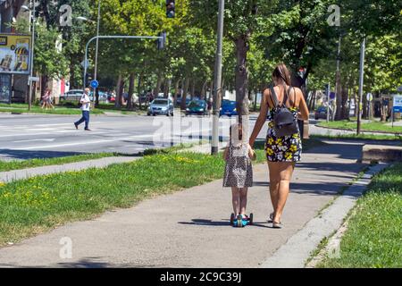 Zrenjanin, Serbia, 29 luglio 2020. Una giovane madre e la sua bambina si rilassarono scendendo per strada. La ragazza impara a guidare uno scooter. Foto Stock