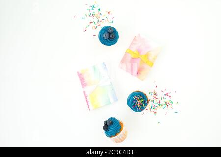 Muffin dolci, confetti caramelli e scatola regalo iridata isolati su sfondo bianco. Disposizione piatta, vista dall'alto Foto Stock