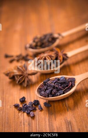 spezie di unghie, anis star e barberry in cucchiai di legno in uno studio Foto Stock
