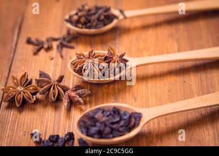 spezie di unghie, anis star e barberry in cucchiai di legno in uno studio Foto Stock