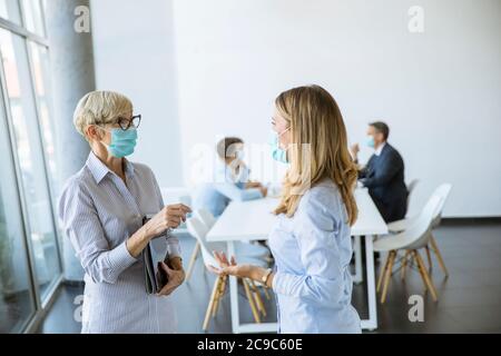 Due uomini d'affari, maturi e giovani, che parlano in ufficio e indossano la maschera come protezione da virus Foto Stock