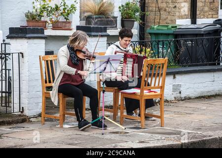 blocco del virus corona, violino e fisarmonica, musicisti locali che intrattengono vicini, socialmente distanziati, scena di strada, Foto Stock