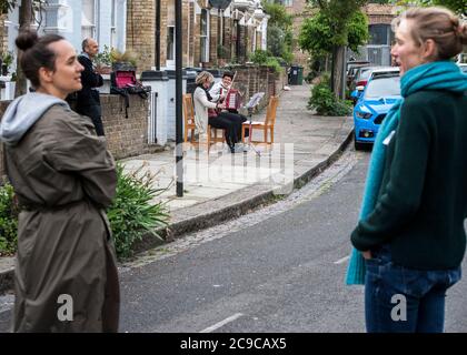 blocco del virus corona, violino e fisarmonica, musicisti locali che intrattengono vicini, socialmente distanziati, scena di strada, Foto Stock