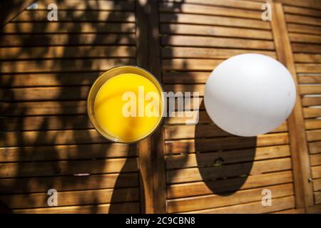 bicchiere di succo d'arancia, tavolo da giardino in legno, accanto alla luce bianca del globo, Foto Stock