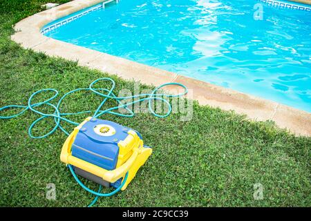 Pulitore automatico piscina con tubo elettrico protetto su erba e piscina appena pulita Foto Stock