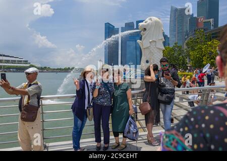 Essendo fotografato di fronte a una statua del Merlion, il simbolo nazionale di Singapore, una creatura mitica con la testa del leone e il corpo di pesci. Foto Stock