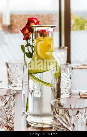 Tavolo posato con caraffa, bicchieri di limonata di cristallo e rose in vaso. Foto Stock