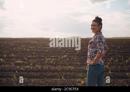 Donna coltivatore in piedi e guardando terreno agricolo Foto Stock