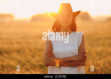 Donna contadina in cappello cowboy a campo agricolo al tramonto con sunflare Foto Stock